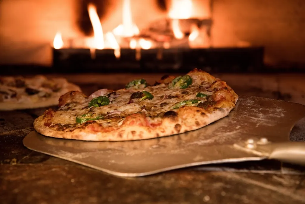 Pizza op een schep voor het vuur van een houtoven